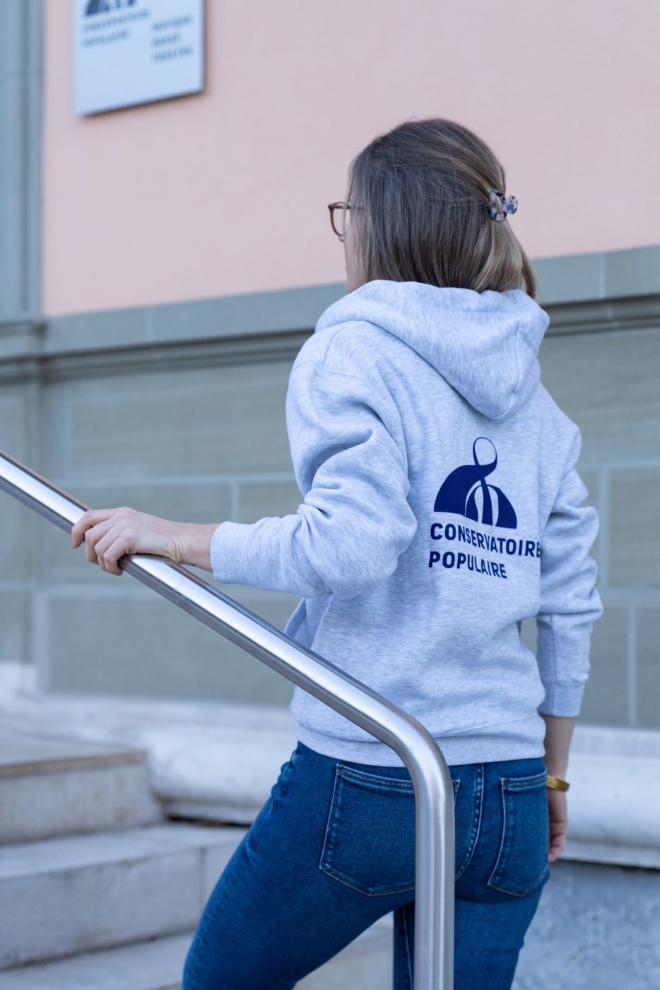 femme de dos avec un pull du conservatoire populaire du genève qui est vendu sur la boutique en ligne